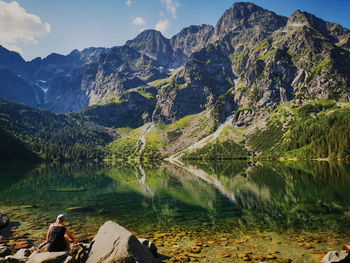 Man sitting on rock by lake against sky