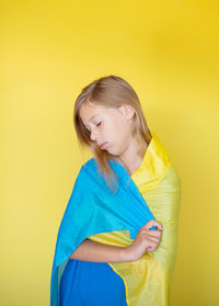 Young woman standing against yellow background