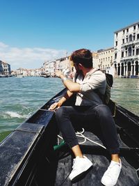 Man sitting on boat in city against sky