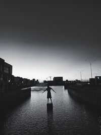 Silhouette man standing on river against sky in city