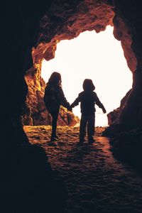 Silhouette children standing in cave against sky