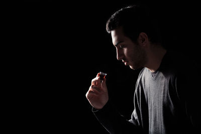 Portrait of young man using smart phone against black background