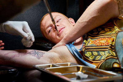 Cropped hands of artist bamboo tattooing on young man arm
