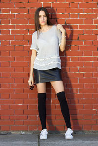 Full length portrait of woman standing against brick wall