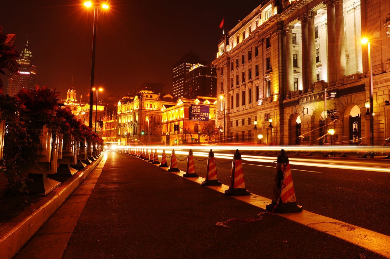 illuminated, building exterior, night, architecture, built structure, city, street light, street, the way forward, lighting equipment, transportation, diminishing perspective, building, road, city street, sky, residential building, city life, residential structure, vanishing point