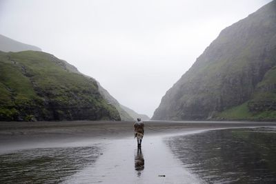 Woman standing on lake by mountains against sky