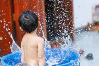 Rear view of shirtless boy in bathtub outdoors