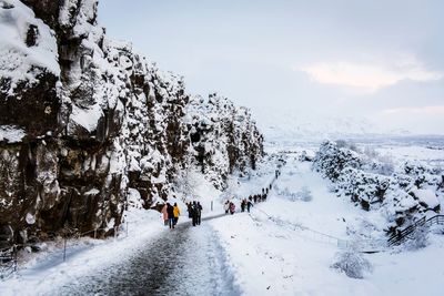 Rear view of people walking on snow covered mountain against sky