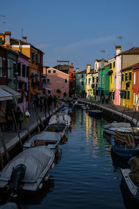 Boats moored in canal by buildings against sky in city