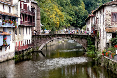 People walking on arch bridge over river amidst residential buildings