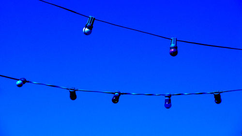 Low angle view of lighting decorations hanging against clear blue sky