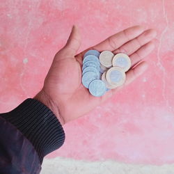 High angle view of hand holding coins against wall