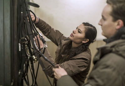 Young couple arranging bridles in horse stable