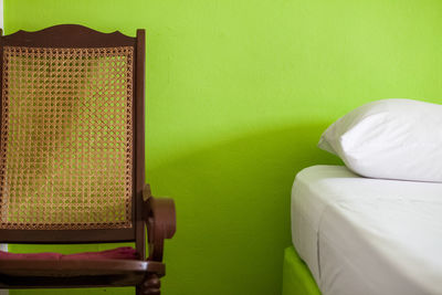 Close-up of wooden chair by bed against green wall at home