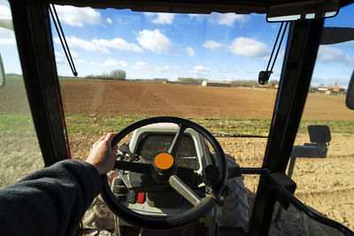 Cropped hand driving tractor on agricultural field