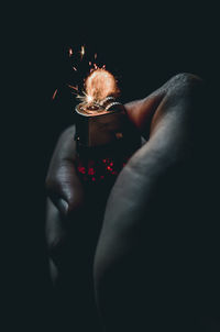 Close-up of hand holding sparkler against black background