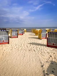 Hooded chairs on beach against sky