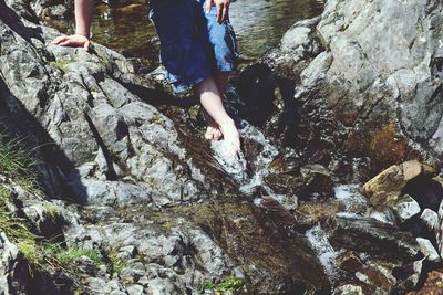 Low section of man standing on stream flowing through rocks at forest