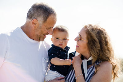 Grandparents smiling & holding grandson on beach