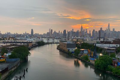 Newtown creek amidst buildings against manhattan skyline during sunset