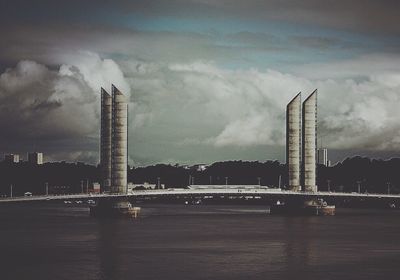 View of city at waterfront against cloudy sky