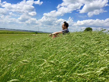 Man sitting by plants in farm against sky