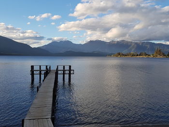Pier on lake by mountains against sky