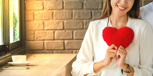 Midsection of woman holding red while sitting on table against wall