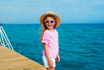 Funny face kid in sunglasses and straw hat posing on sea shore