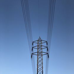 Low angle view of electricity pylon against clear blue sky