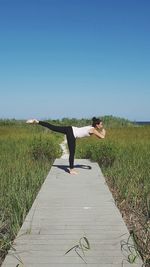 Woman exercising on boardwalk against clear blue sky