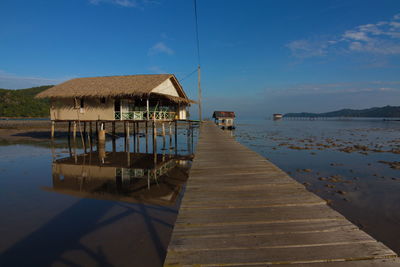 Wooden pier on lake by houses against sky