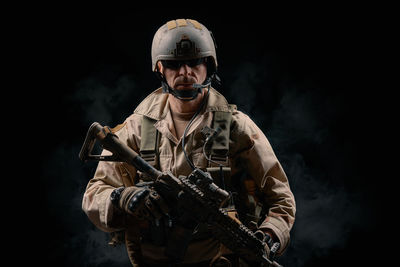 Man wearing helmet holding rifle against black background