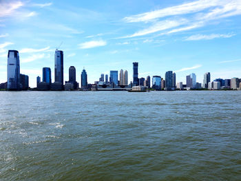 Sea by modern buildings in city against sky