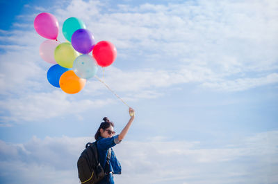 Low angle view of man holding balloons against sky