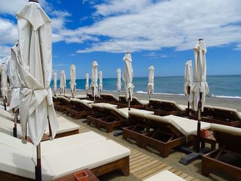 Lounge chairs by swimming pool at beach against sky