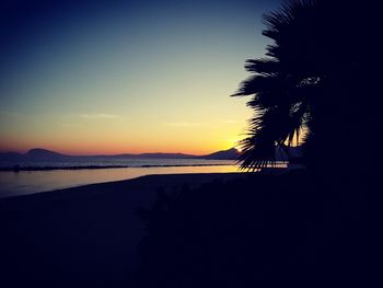 Silhouette palm trees on beach against clear sky at sunset