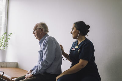 Mature female healthcare worker examining senior patient sitting in clinic