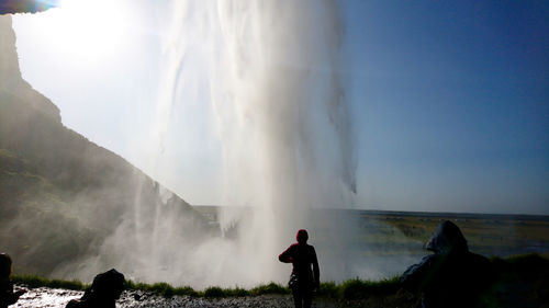 Rear view of people looking at waterfall against sky