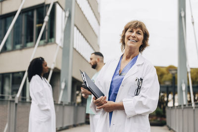 Happy mature female doctor looking away while colleagues in background