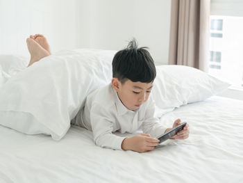 Cute boy using phone while lying on bed at home