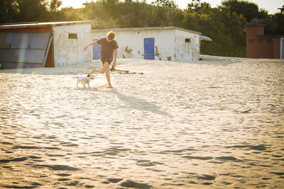 Boy with dog running on sand at beach during sunny day