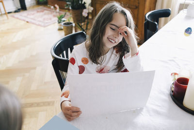 Happy girl with paper sitting at dining table