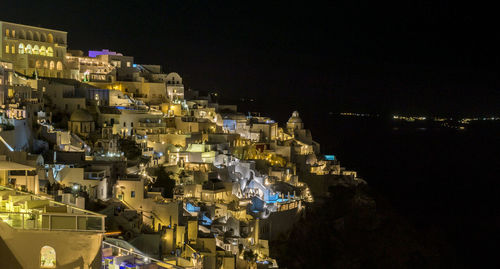 Illuminated residential district by sea against sky at night