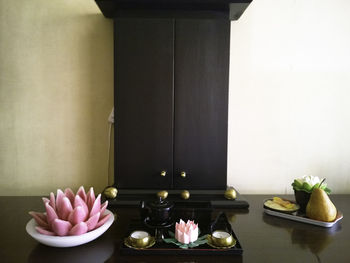 Teddy bear and artificial flowers on table against wall