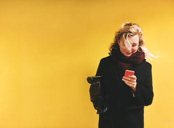 Happy beautiful woman using phone against yellow background