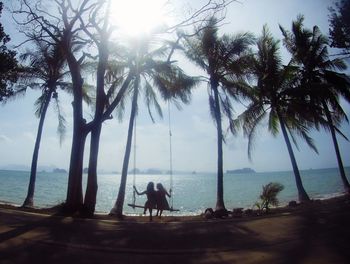 People relaxing on palm tree by sea against sky