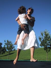 Mother and son jumping on trampoline against clear sky