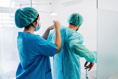 Back view of vet doctors putting on protective uniform and gloves while standing in bright operating theater of veterinarian hospital and preparing for surgery