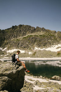 Side view of man on rock by lake against sky